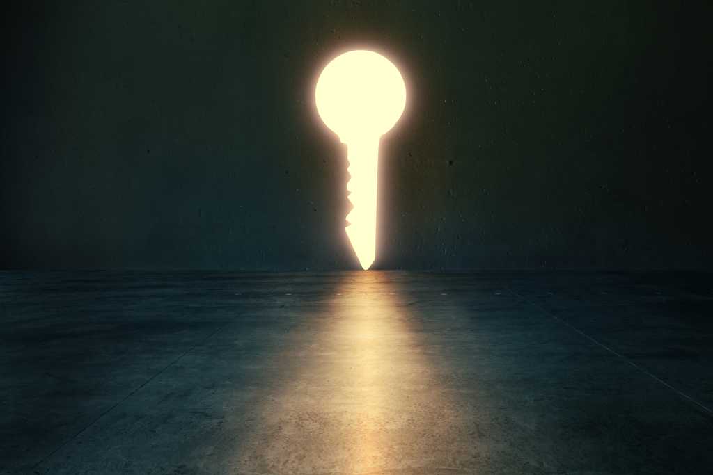 3811558-0-90516200-1742228020-shutterstock_2468143481-1 Light glows through key shaped hole in dark empty room. Golden key concept