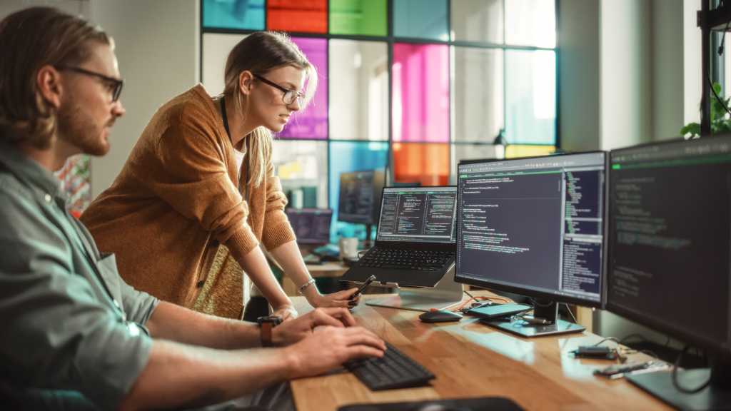 3544514-0-49365900-1742465512-shutterstock_2216535703-1 Male Data Scientist and Female Developer Working With Errors in Code on Desktop Computer in Creative Office. Caucasian Man and Woman Succesfully Fixed a Software Bug And High Five Each Other.