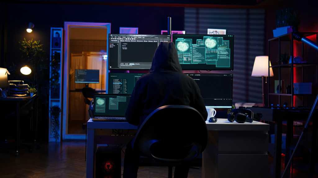 3849245-0-09428000-1742384563-shutterstock_2477533867-1 Hacker arriving in secret base with laptop, ready to start programming viruses. Scammer in criminal den opening notebook to exploit network servers and bypass security measures, camera B