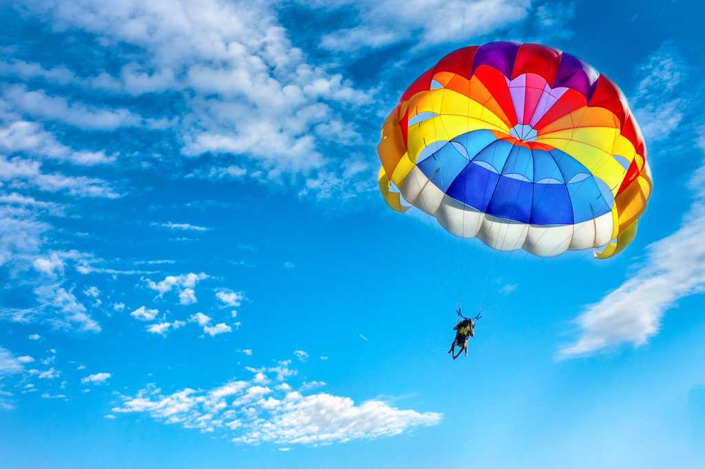 3956262-0-82073900-1744057349-shutterstock_1018105807-100936711-orig-1 shutterstock 1018105807 rainbow colored parachute against a blue sky and cirrus clouds