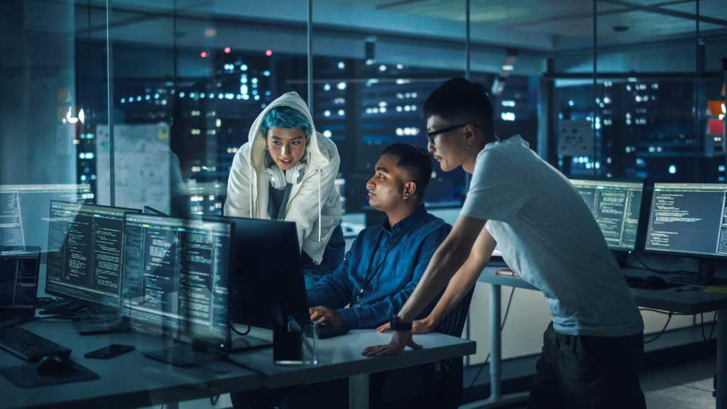 3963136-0-67091400-1745830927-shutterstock_2083365991-1 Diverse Team of Professionals Meeting in Office at Night: Brainstorming IT Programmers Use Computer Together, Talk Strategy, Discuss Planning. Software Engineers Develop Inspirational App Program