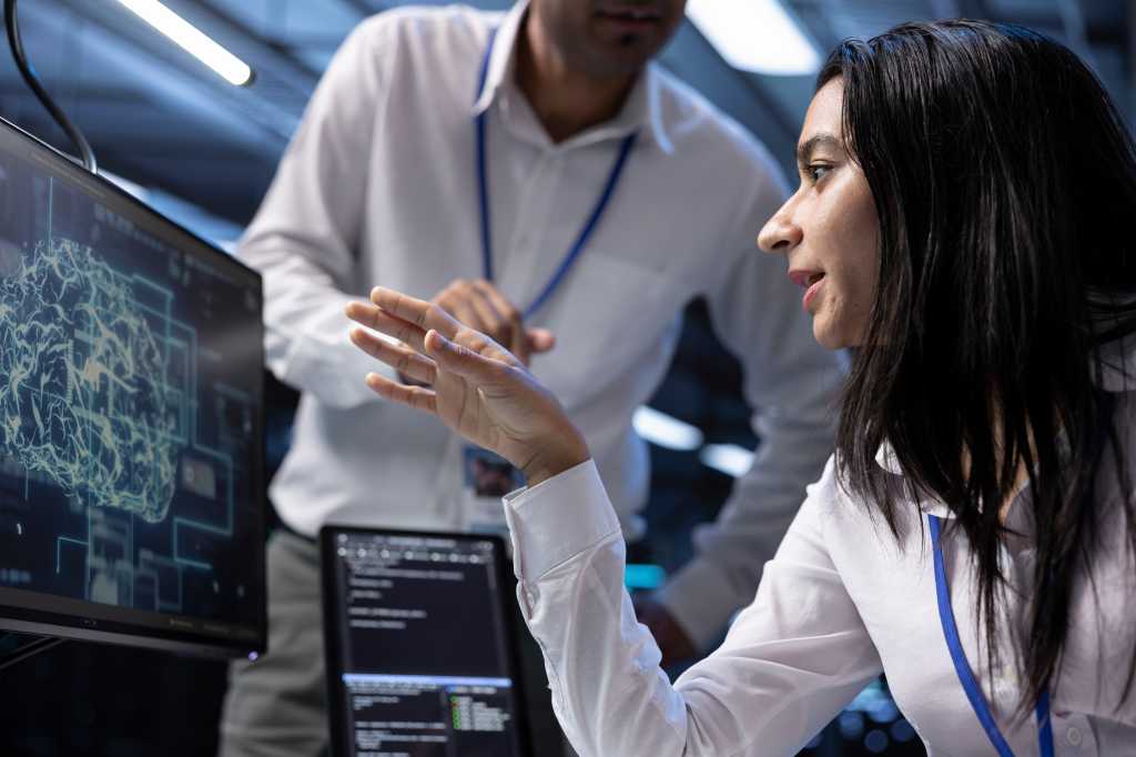 3972688-0-31374200-1745917436-shutterstock_2515682037-1 Coworkers using AI tech to fix errors in server farm providing storage. IT staff members in data center using PC to enable artificial intelligence to process datasets for training