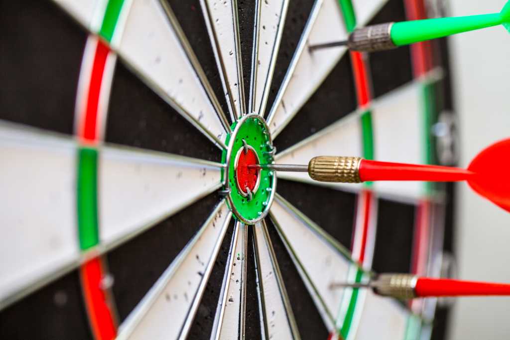 3973969-0-28734400-1746435689-shutterstock_424700656-1 close up of dartboard and red and green darts with bullseye hits and misses
