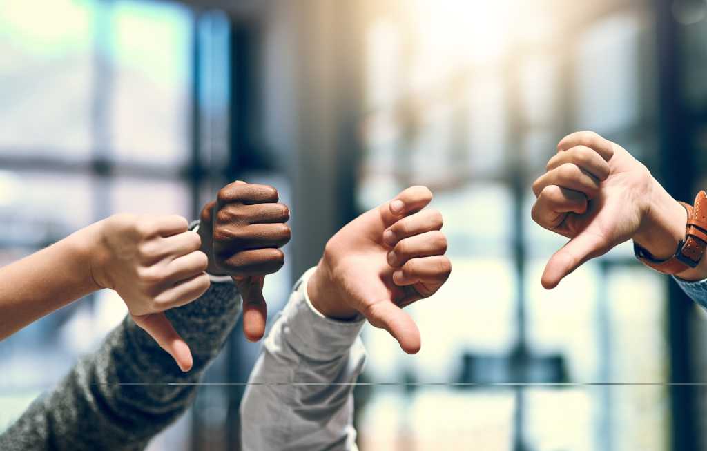 3975732-0-05606700-1746141786-shutterstock_2500133623-1 four hands raised with thumbs down in front of window with blurred light