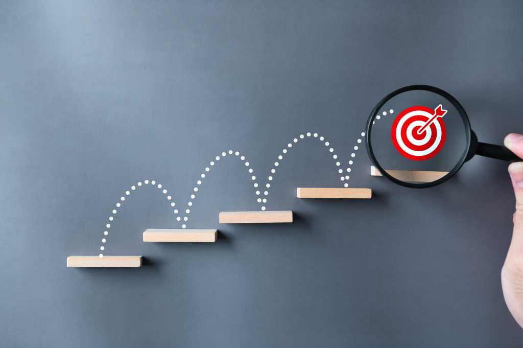 3977605-0-95039300-1746608585-shutterstock_2322629679-1 Step-by-step: a series of steps with a bulls-eye target on the top step.