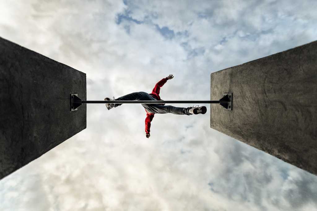 3998221-0-52203200-1749459674-shutterstock_1277815804-1 man jumps over obstacle, parkour leaps across gap, view from below looking up at cloud filled sky