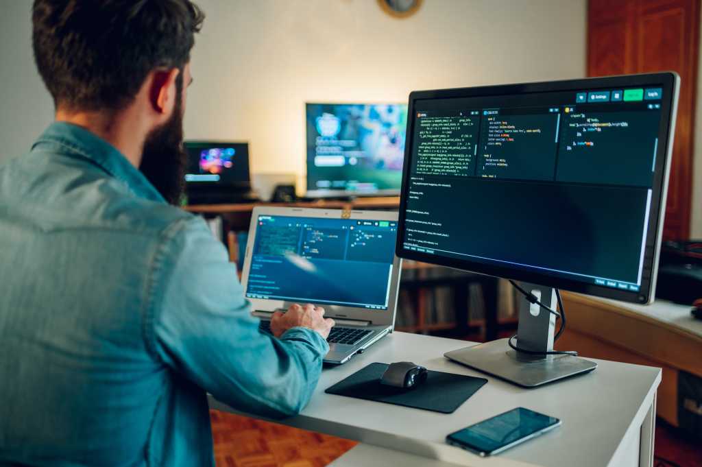 4003637-0-72333600-1749492095-shutterstock_2300957969-1 Back view of a senior developer typing code and programming a new generation of AI bots and AI generators at the home office. Artificial intelligence development and programming AI bots.