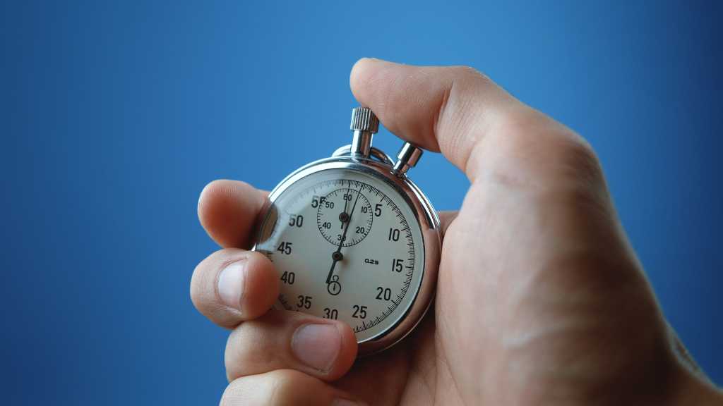 Hand holding an analog stopwatch on a blue background. Speed, efficiency, performance.