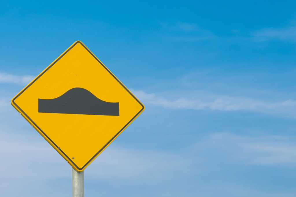 Yellow and black "speed bump" signage against a blue-sky background.