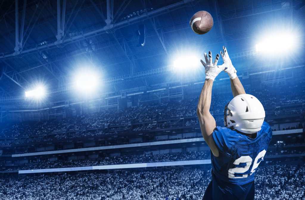 American football player catching a touchdown pass under the lights in a large stadium.