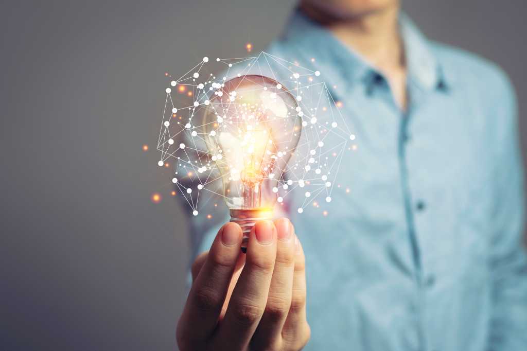 Person in blue shirt extends a lightbulb toward the screen. Ideas, innovation.